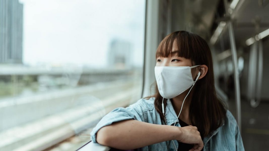 girl with white mask and headphones watching view from train