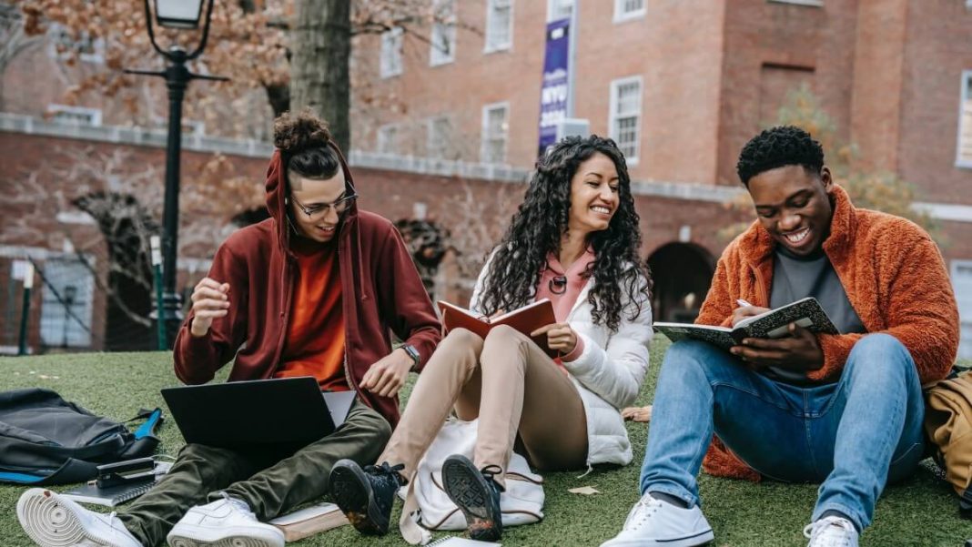 students with books sitting on park near college building