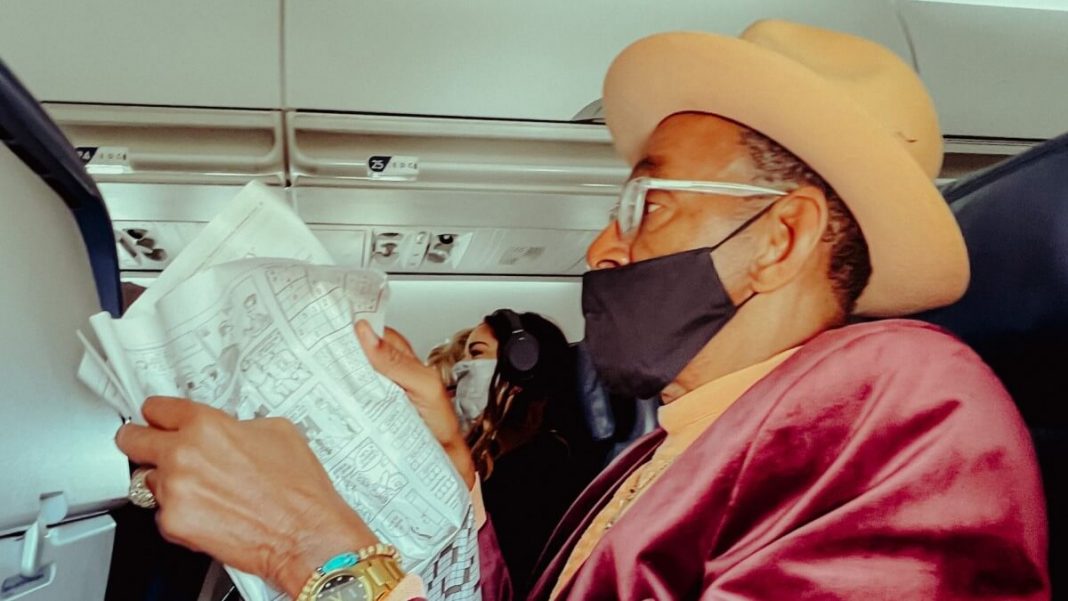 old airplane passenger wearing mask reading newspaper