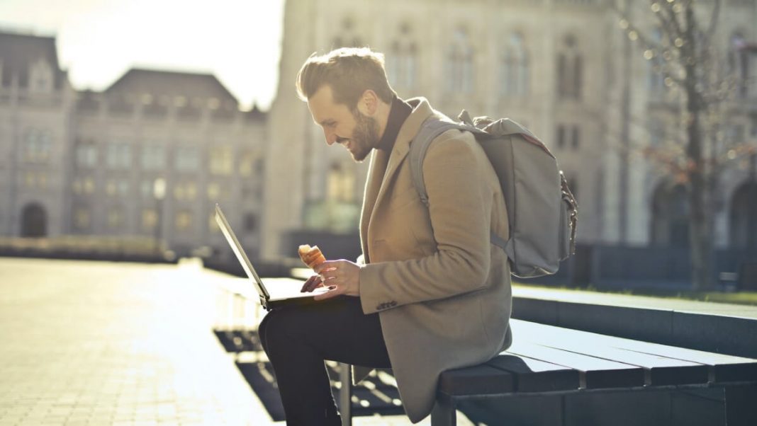 freelancer man with backpack and coat holding laptop
