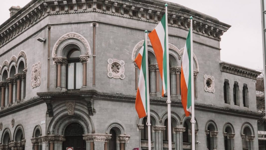 ireland flags on flagpoles in front of grey buildings
