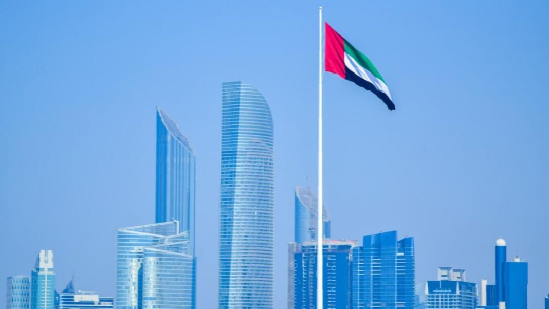uae flag waving on flagpole with dubai skyscrapers in the background
