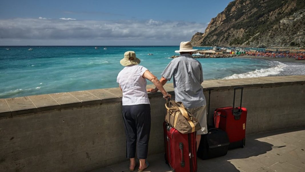 old tourist couple with red luggages looking at sea beach view